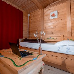 Chalet en bois douillet avec lit simple et décor coloré, idéal pour un séjour unique.