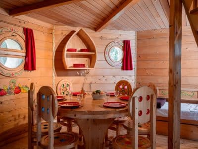 Cabane en bois colorée avec un coin repas chaleureux et des fenêtres rondes.