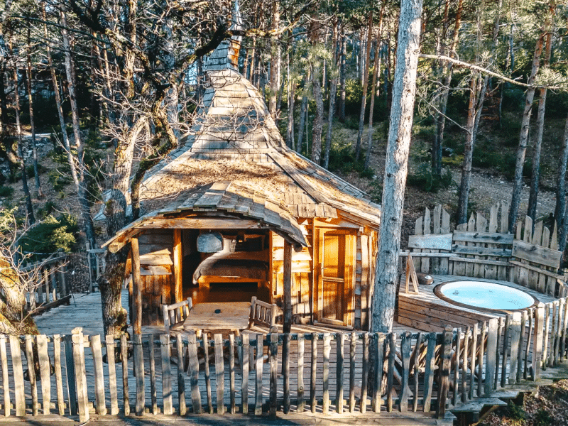 Cabane en bois perchée dans les arbres, avec un jacuzzi extérieur entouré de nature.