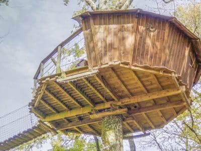 Cabane perchée en bois, suspendue dans les arbres, offrant une vue panoramique.
