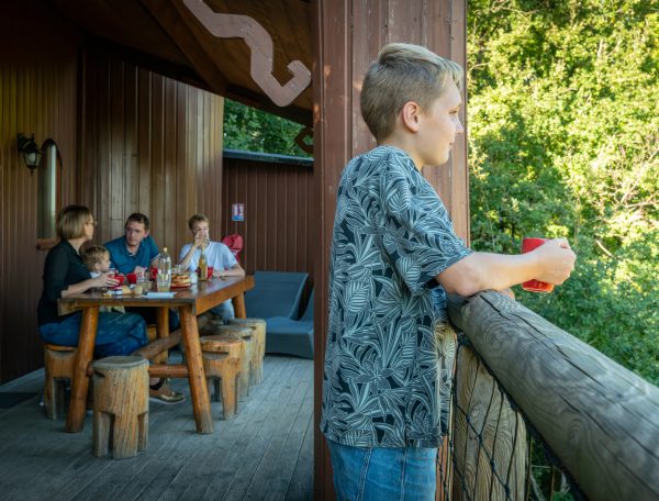 Chalet en bois avec terrasse, famille réunie autour dune table en extérieur.