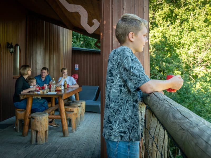 Chalet en bois avec terrasse, famille réunie autour dune table en extérieur.