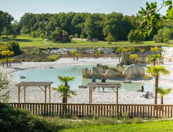 Hébergement touristique avec plage de sable, palmiers et rochers naturels.