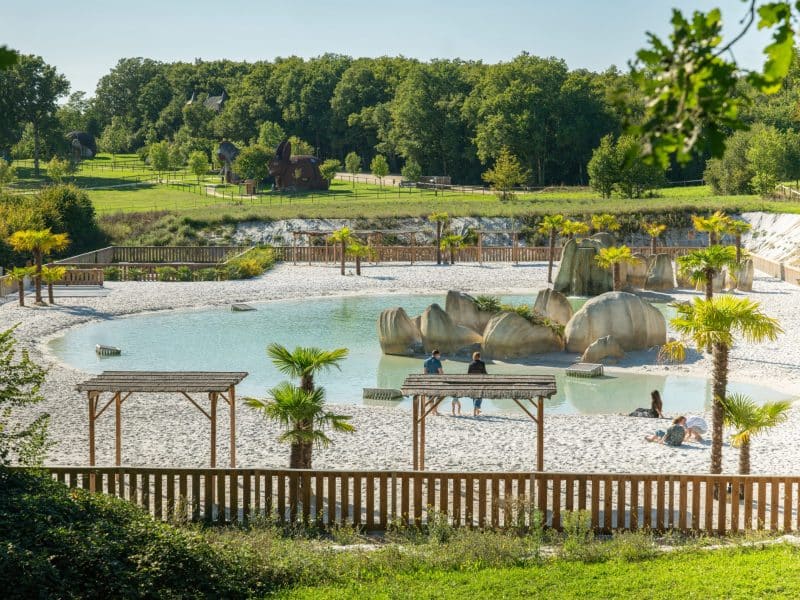 Hébergement touristique avec plage de sable, palmiers et rochers naturels.