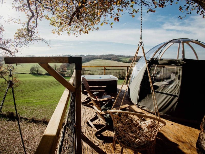 Cabane dans les arbres avec jacuzzi, vue panoramique sur la campagne verdoyante.