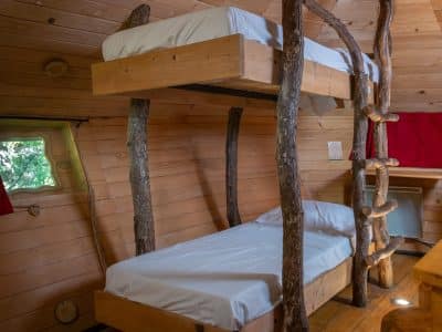 Cabane en bois avec lits superposés et échelle en troncs darbres, ambiance chaleureuse.