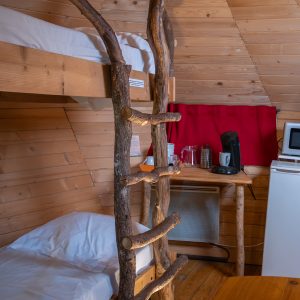 Hébergement insolite en cabane, avec lits superposés en bois et kitchenette équipée.