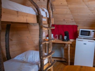 Hébergement insolite en cabane, avec lits superposés en bois et kitchenette équipée.