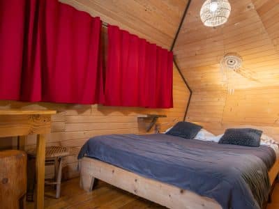 Cabane en bois à Nouvelle-Aquitaine, avec un lit douillet et des rideaux rouges.