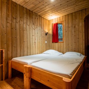 Chalet en bois chaleureux avec lit double et lumière douce, idéal pour un séjour paisible.