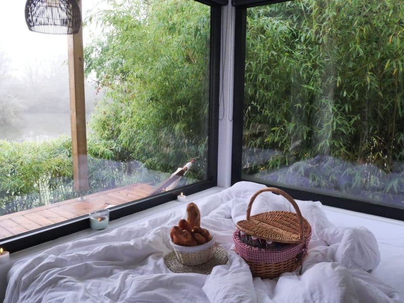 Chalet moderne avec vue sur la nature, lit douillet et panier de viennoiseries.
