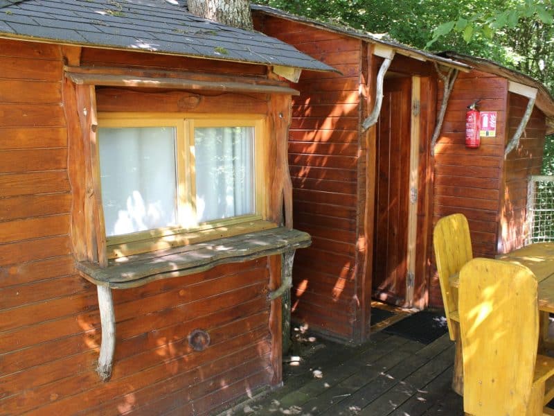 Cabane en bois dans les arbres, avec une terrasse en bois et des détails naturels.