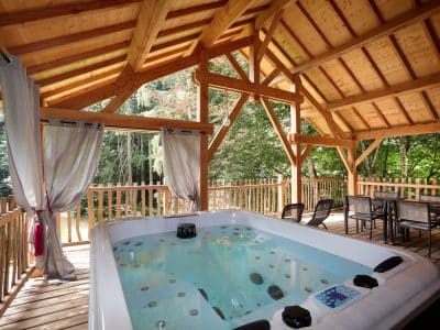 Cabane en bois avec jacuzzi, entourée de verdure en Auvergne-Rhône-Alpes.