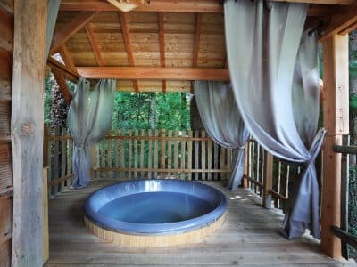 Cabane perchée en bois avec jacuzzi, entourée de verdure apaisante.