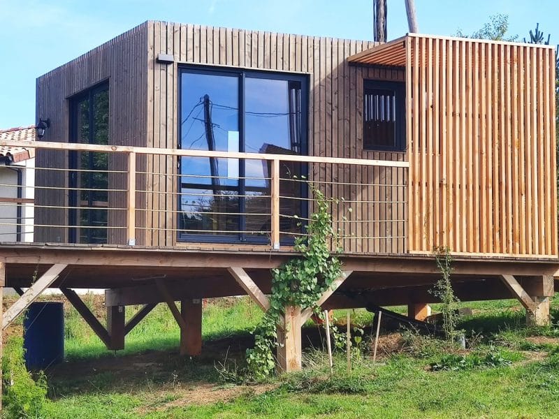Cabane en bois sur pilotis avec grandes fenêtres, entourée de verdure en Auvergne.