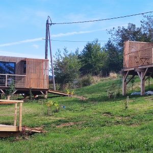 Hébergement insolite : cabane en bois avec terrasse, entourée de verdure.