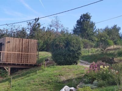 Cabane en bois sur pilotis, entourée de verdure et de fleurs colorées.