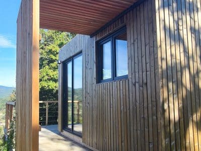 Cabane en bois moderne avec terrasse, vue dégagée sur la nature en Auvergne-Rhône-Alpes.