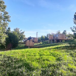 Cabane en bois perchée, entourée de verdure et sous un ciel bleu clair.