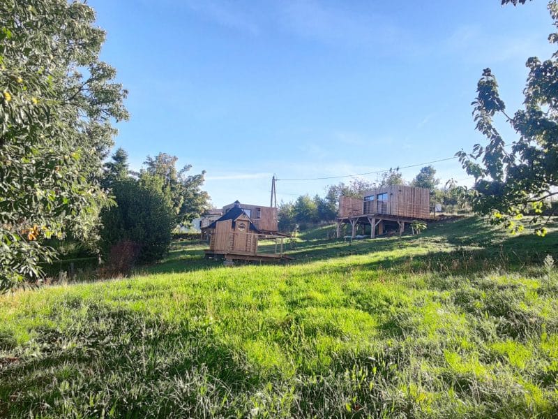 Cabane en bois perchée, entourée de verdure et sous un ciel bleu clair.