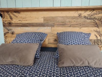 Chambre en bois avec tête de lit artisanale et coussins douillets en Auvergne-Rhône-Alpes.