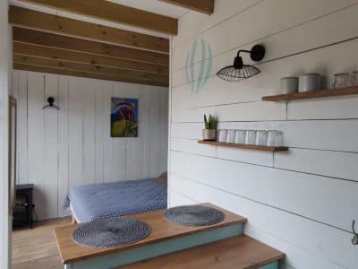 Hébergement insolite en Auvergne-Rhône-Alpes, intérieur lumineux avec lit et étagères en bois.