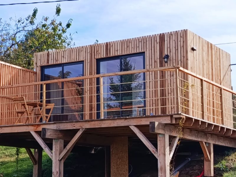 Cabane en bois sur pilotis avec terrasse, offrant une vue sur la nature en Auvergne.