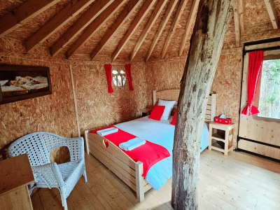 Cabane en bois avec un lit confortable et des rideaux rouges, ambiance chaleureuse.
