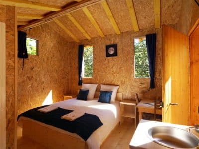 Chalet en bois chaleureux avec lit double et fenêtres lumineuses en Auvergne-Rhône-Alpes.