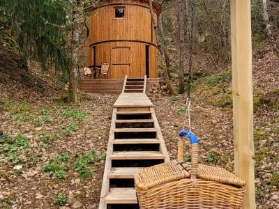 Cabane en bois perchée, accessible par un escalier, entourée de verdure.