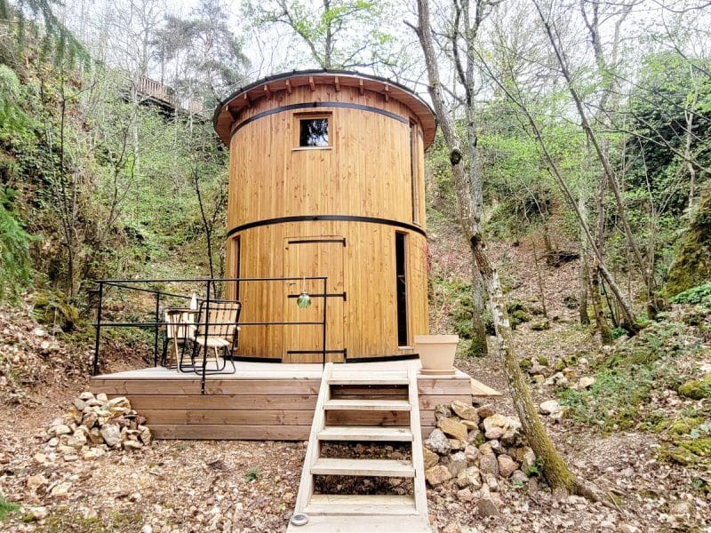 Cabane en bois perchée, entourée de verdure, avec une terrasse en bois accueillante.