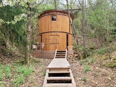 Cabane en bois ronde, nichée dans la forêt, avec une terrasse en bois accueillante.