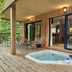 Cabane en bois en Bretagne avec jacuzzi et terrasse en bois entourée de verdure.