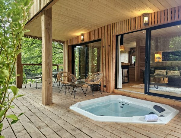 Cabane en bois en Bretagne avec jacuzzi et terrasse en bois entourée de verdure.