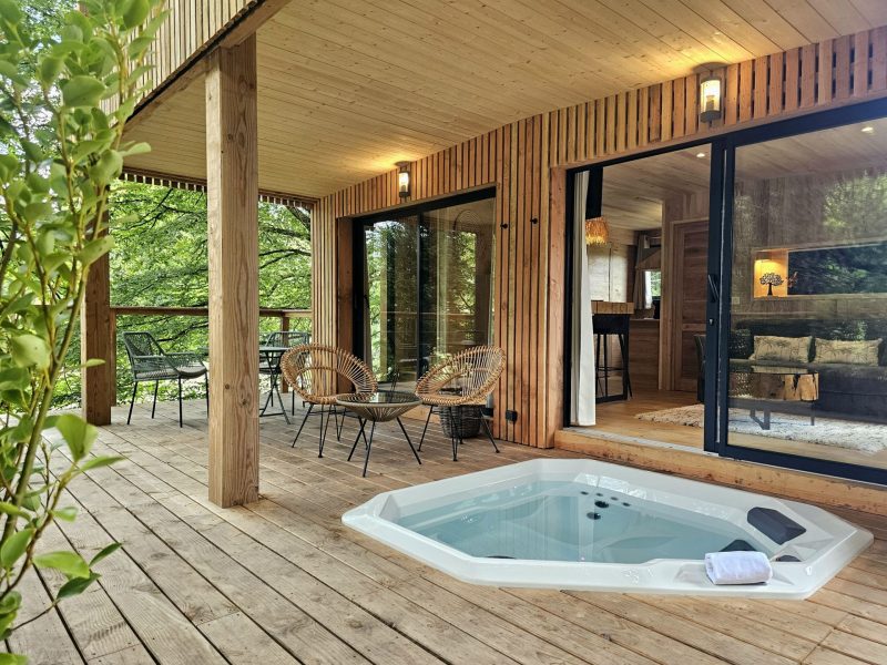 Cabane en bois en Bretagne avec jacuzzi et terrasse en bois entourée de verdure.
