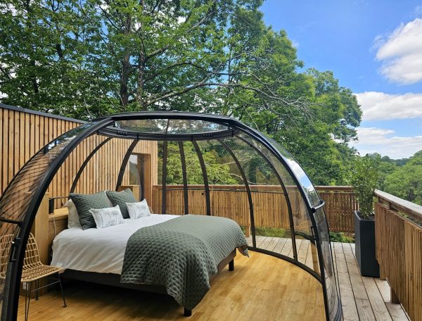 Cabane moderne avec lit douillet, entourée de verdure et vue dégagée.