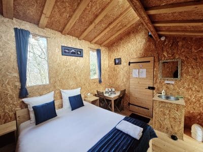 Cabane en bois cosy avec lit double, fenêtres lumineuses et décoration naturelle.