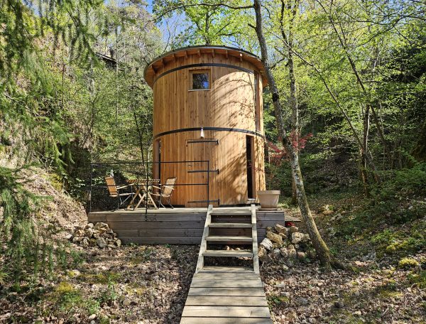 Cabane en bois ronde, entourée de verdure, avec terrasse et mobilier extérieur.