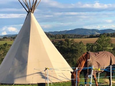 Teepee en pleine nature avec un cheval paissant, vue sur les montagnes.