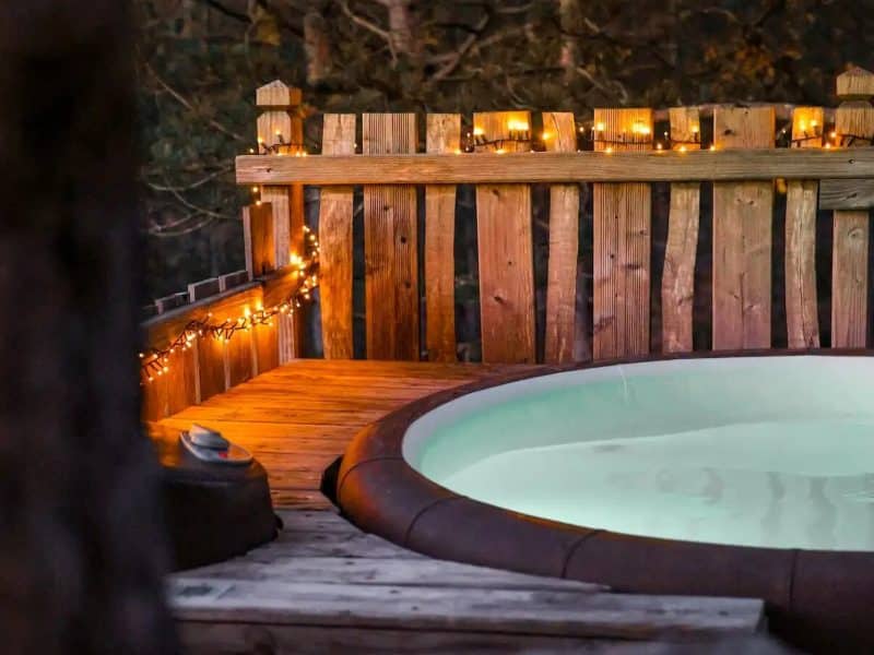 Cabane en bois avec un jacuzzi illuminé, entourée de nature paisible.