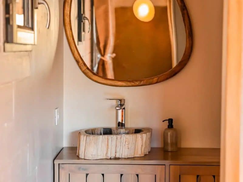 Salle de bain dun hébergement en bois, avec un lavabo en pierre et un miroir organique.