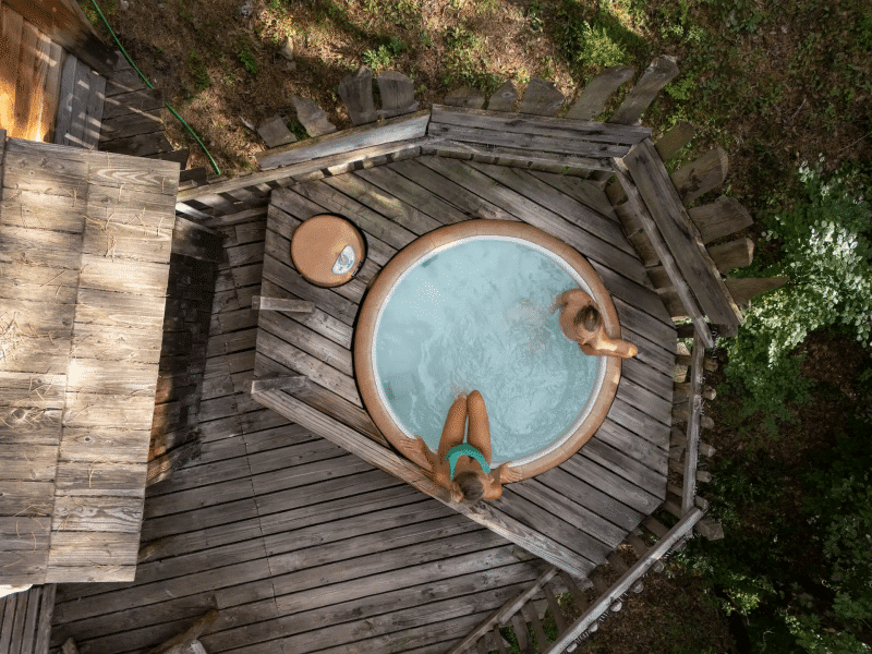 Cabane en bois avec jacuzzi extérieur entouré de verdure. Moments de détente garantis.