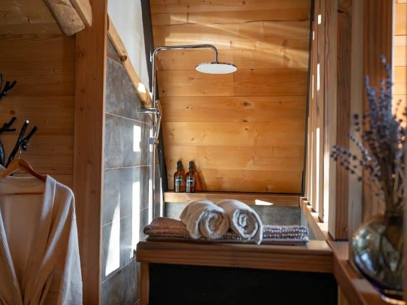 Chalet en bois avec salle de bain moderne, douche à effet pluie et serviettes douces.
