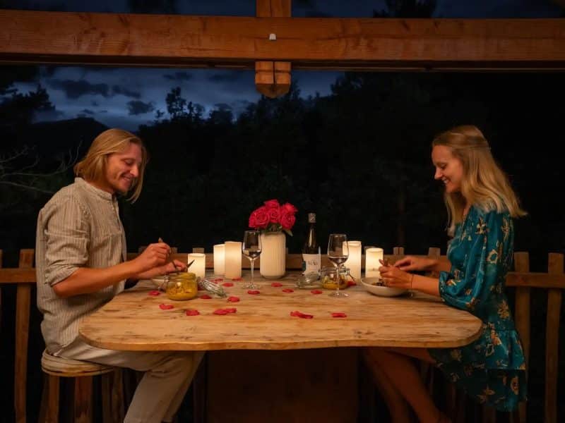 Dîner romantique en cabane, décoré de roses et bougies, ambiance chaleureuse.