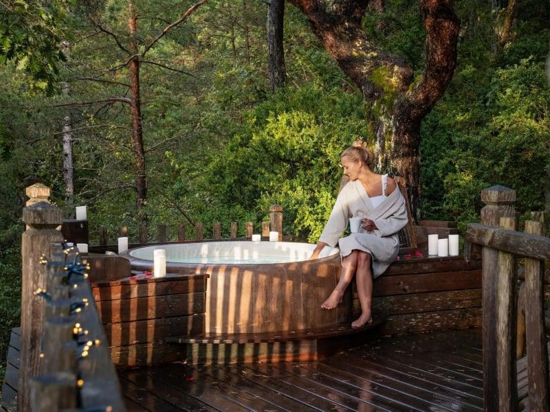 Cabane en bois avec jacuzzi extérieur, entourée de verdure apaisante.