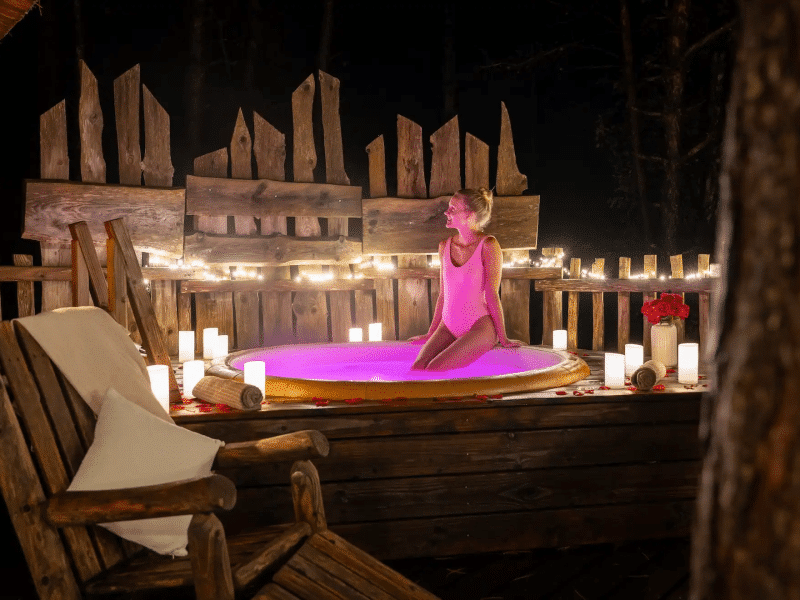 Cabane romantique avec jacuzzi illuminé, ambiance nocturne et décor floral.
