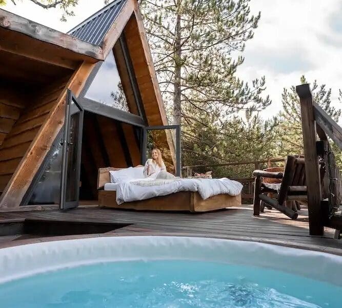 Chalet moderne avec jacuzzi, entouré de nature et vue sur les arbres.