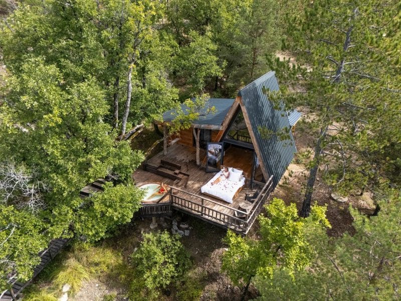Cabane en bois perchée, entourée darbres, avec une terrasse accueillante.