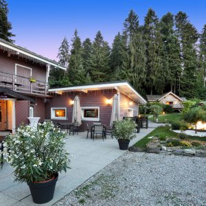 Chalet en bois avec terrasse, entouré de verdure et de fleurs, idéal pour se détendre.