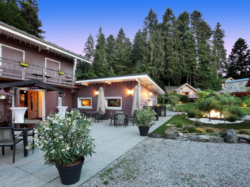 Chalet en bois avec terrasse, entouré de verdure et de fleurs, idéal pour se détendre.